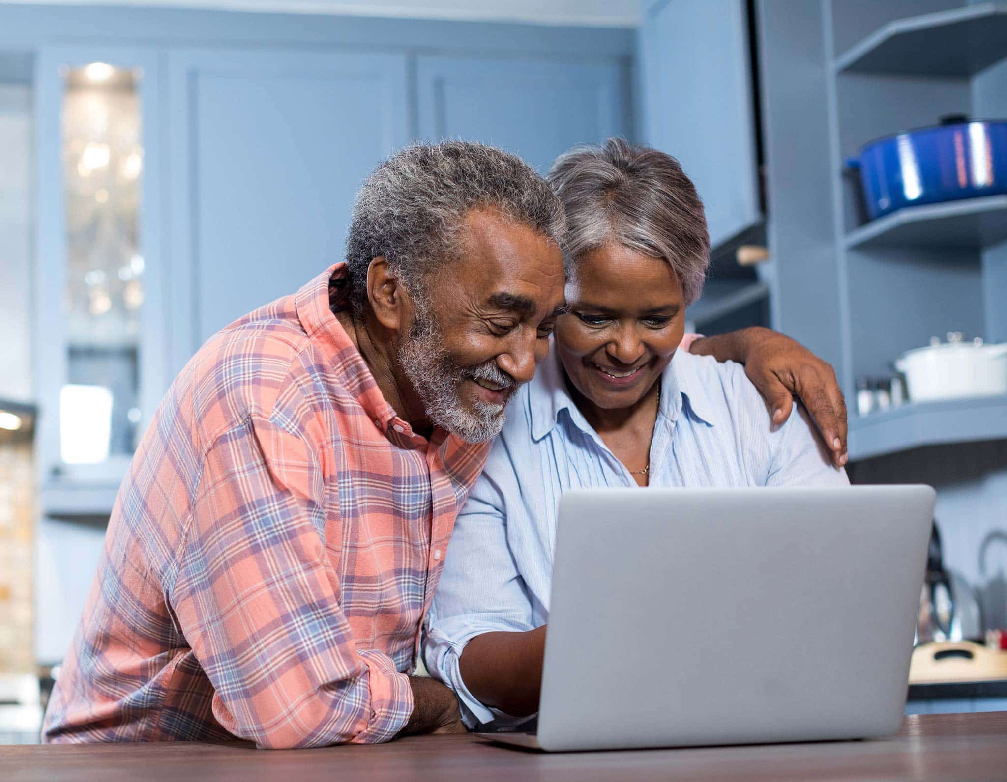 A senior couple sitting together at a counter looking at a laptop